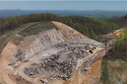 Drone view of Route 58 expansion. Photo shows a steep cut into a hill with rocks scattered in the valley below. There are gentle rolling hills in the background.